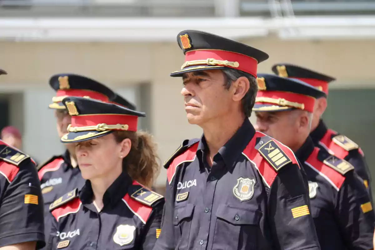 Un grupo de policías con uniformes negros y gorras rojas y negras en formación.