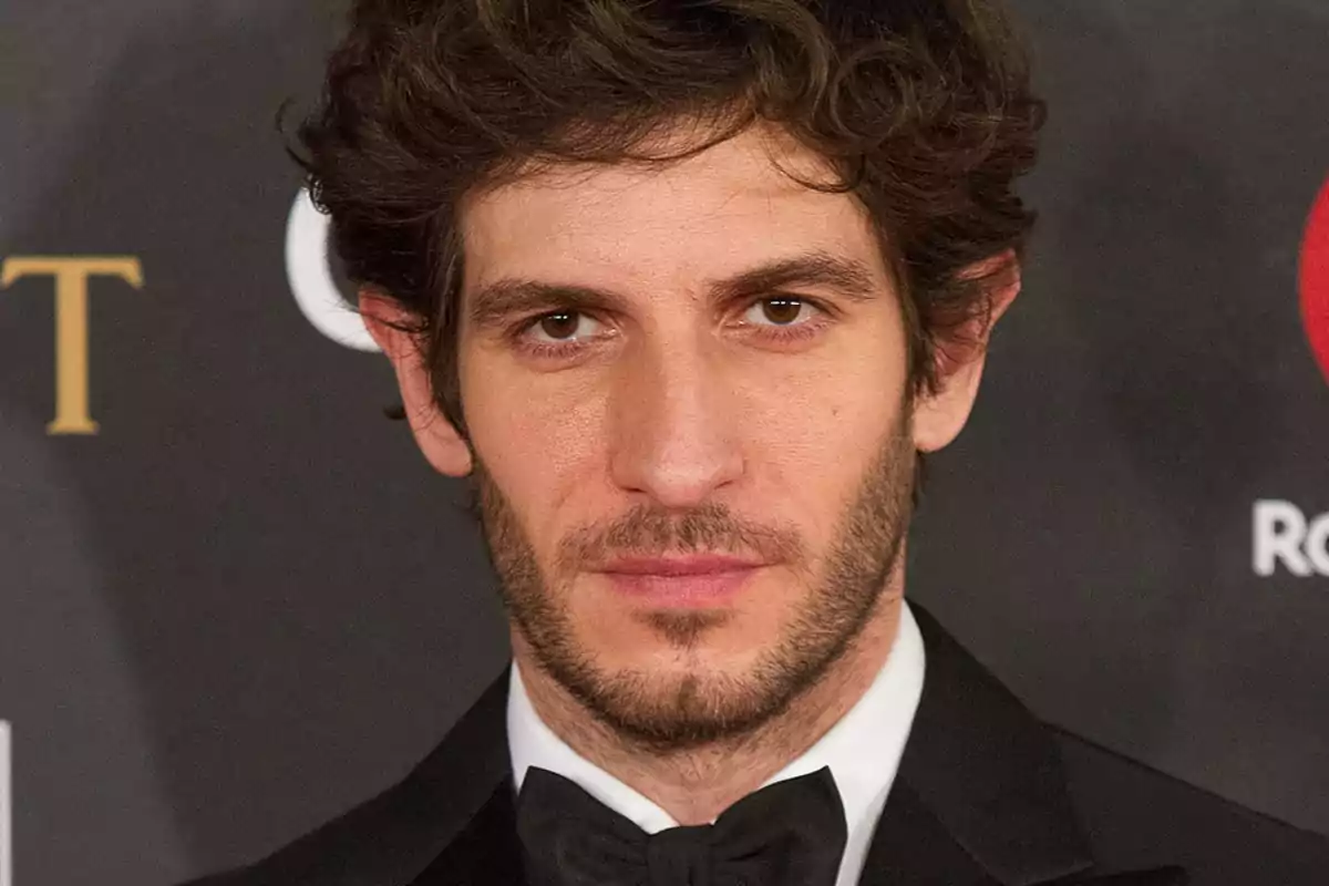 Un home amb barba i cabell arrissat porta un esmòquing negre i corbata de monyo en un esdeveniment formal. Un home amb barba i cabell arrissat porta un esmòquing negre i corbata de monyo en un esdeveniment formal.