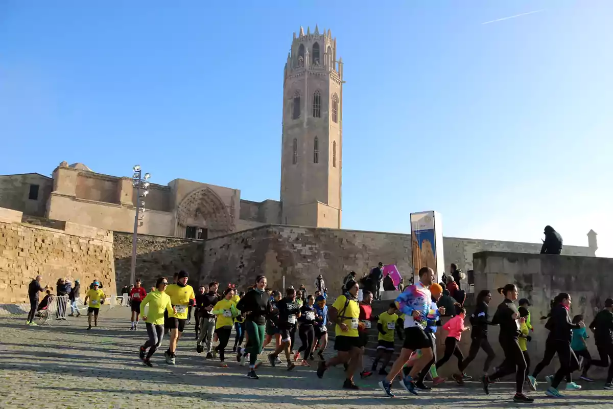 Grupo de corredores participando en una carrera frente a un edificio histórico con una torre alta bajo un cielo despejado.