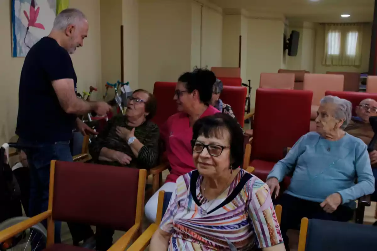 Un grup de persones grans assegudes en una sala mentre un home hi interactua.