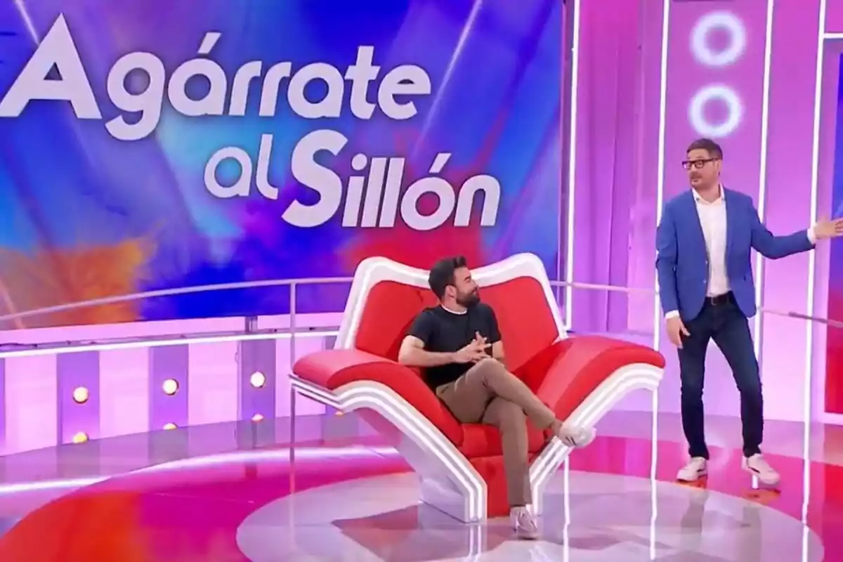 Rafa Castaño i Eugeni Alemany en un plató de televisió acolorit amb un sofà vermell en forma de mà i un rètol gran que diu Agafa’t al Sofà Rafa Castaño i Eugeni Alemany en un plató de televisió acolorit amb un sofà vermell en forma de mà i un rètol gran que diu Agafa’t al Sofà