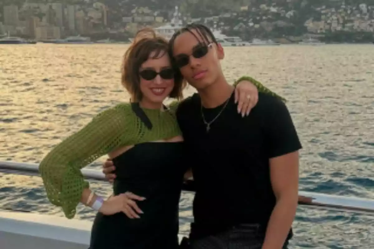 Medium shot of Jazmin Grimaldi and Alexandre Grimaldi, posing embraced on the deck of a boat with the sea and a city in the background at sunset. Medium shot of Jazmin Grimaldi and Alexandre Grimaldi, posing embraced on the deck of a boat with the sea and a city in the background at sunset.
