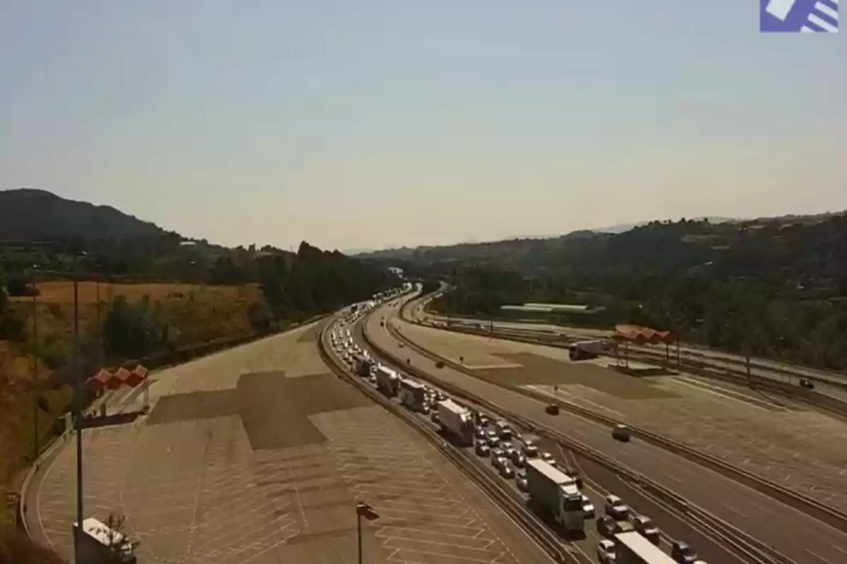 Carretera amb trànsit dens de camions i cotxes en una zona de peatge envoltada de turons i vegetació