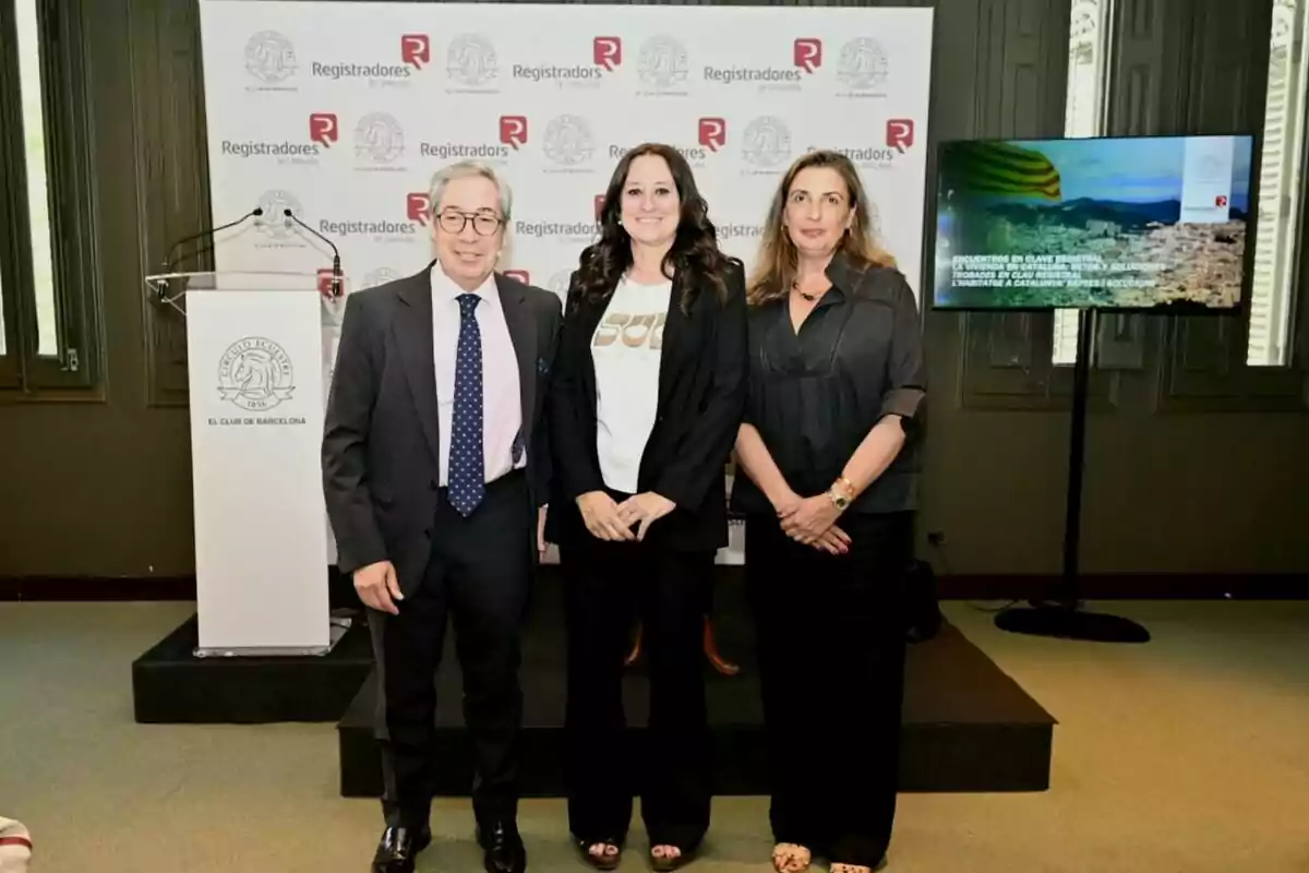 Tres persones posen somrients davant d’un fons amb logotips de Registradors de Catalunya i El Club de Barcelona en un esdeveniment professional. Tres persones posen somrients davant d’un fons amb logotips de Registradors de Catalunya i El Club de Barcelona en un esdeveniment professional.