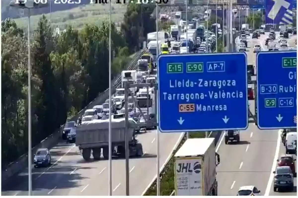 Trànsit dens en una autopista amb diversos carrils i senyals viàries blaves que indiquen direccions cap a Lleida, Saragossa, Tarragona, València i Manresa, a més de la presència de camions i cotxes aturats.