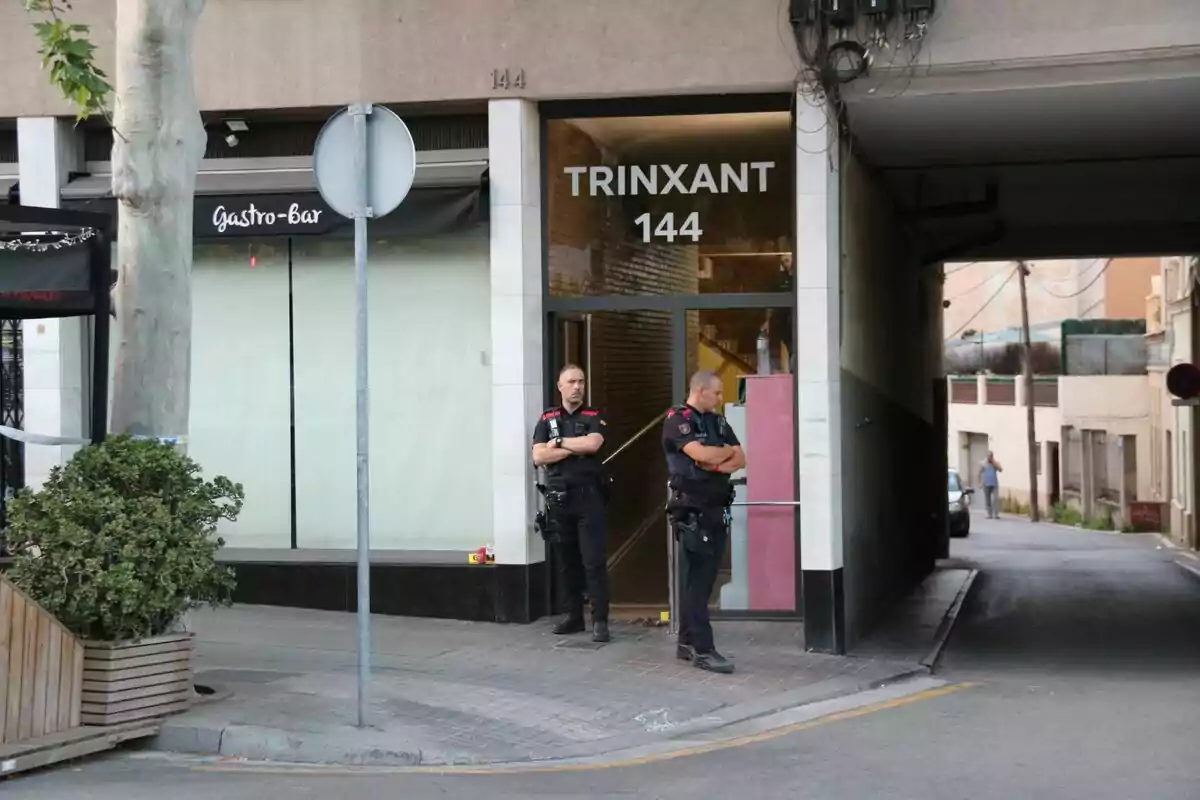Dos policies uniformats estan drets a l’entrada d’un edifici amb el rètol Trinxant 144 en una cantonada del carrer. Dos policies uniformats estan drets a l’entrada d’un edifici amb el rètol Trinxant 144 en una cantonada del carrer.