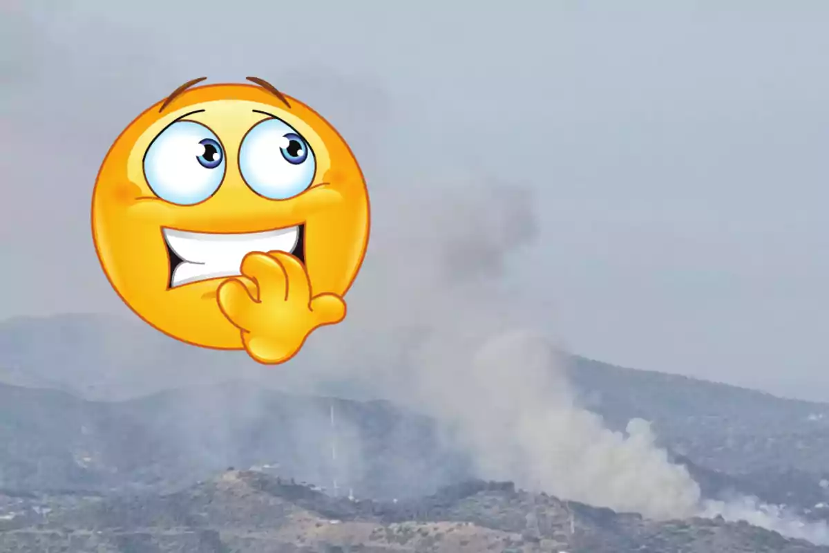 Un emoticona nerviosa sobre una imatge de fum sortint d’una zona muntanyosa