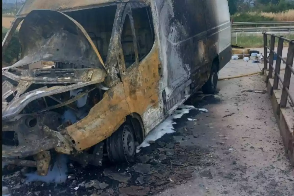 Furgoneta completament calcinada i danyada després d’un incendi, estacionada al costat d’una barana en una carretera