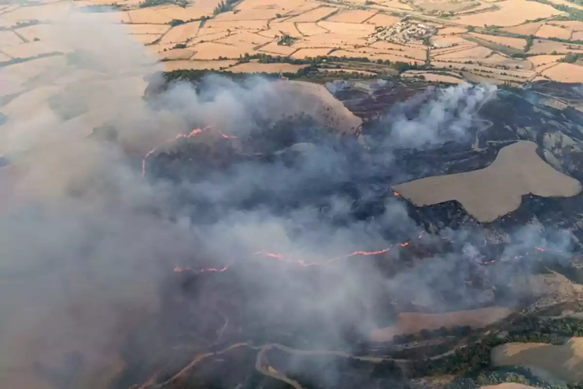 Vista aèria d’un incendi forestal en una zona rural amb camps agrícoles i fum cobrint gran part del paisatge