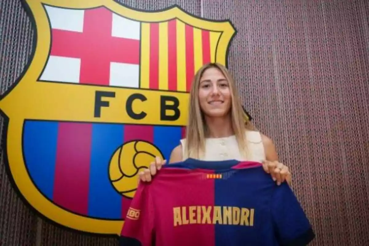 Una dona somrient sosté una samarreta del FC Barcelona amb el nom Aleixandri davant de l’escut del club