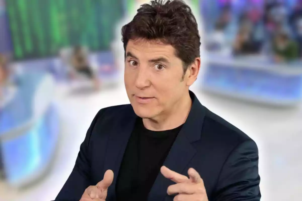 Home de cabells foscos amb jaqueta blau marí assenyalant amb totes dues mans en un estudi de televisió desenfocat