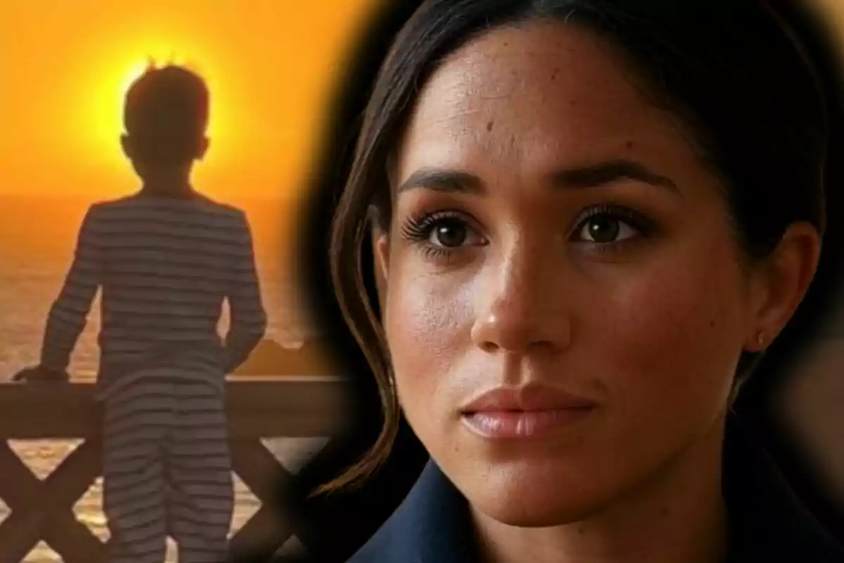Primer pla de Meghan Markle seriosa mirant cap endavant mentre al fons es veu la silueta d’un nen —que és l’Archie, el seu fill— d’esquena observant la posta de sol vora el mar.