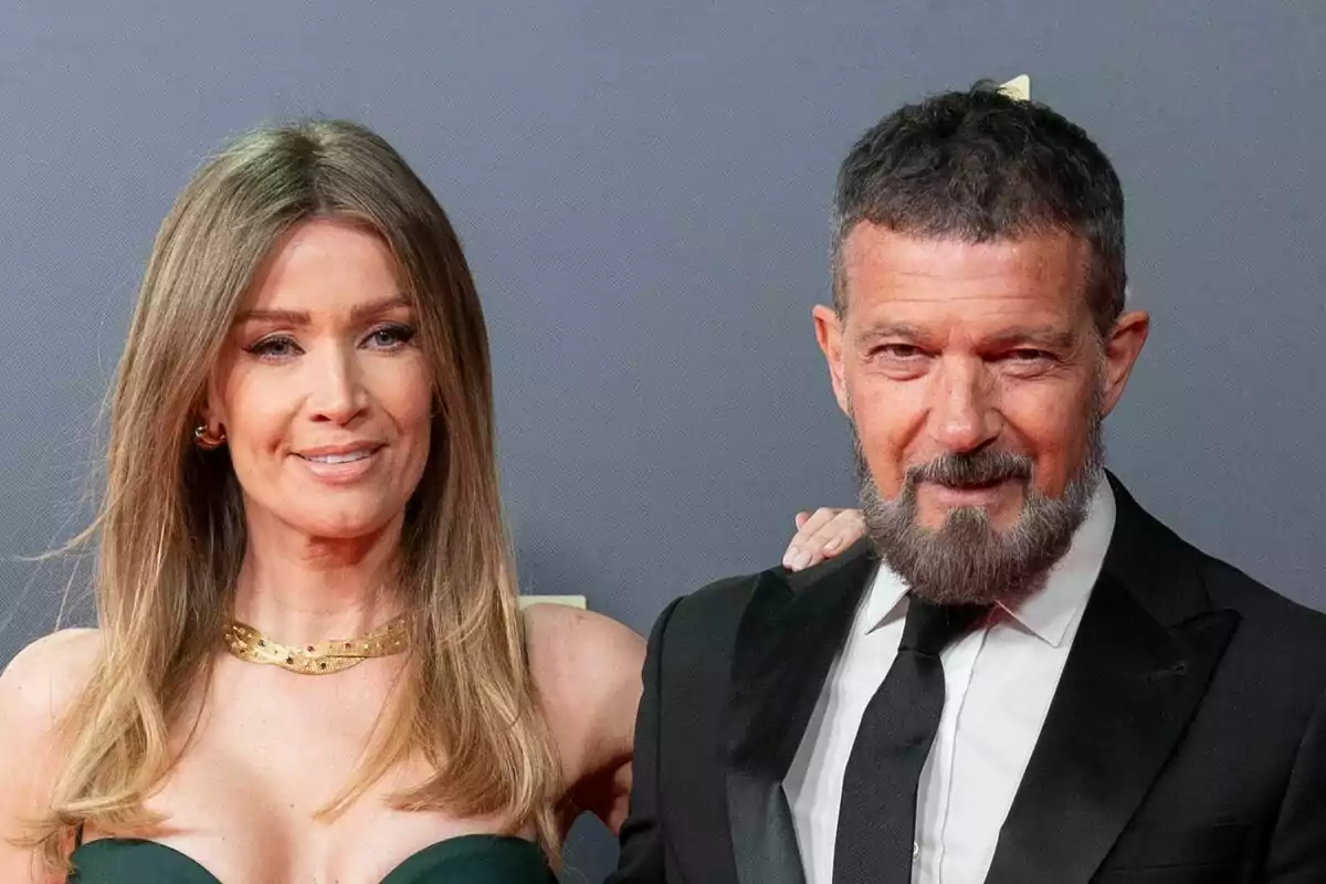 Nicole Kimpel y Antonio Banderas elegantemente vestida posa sonriente en una alfombra roja frente a un fondo gris Nicole Kimpel y Antonio Banderas elegantemente vestida posa sonriente en una alfombra roja frente a un fondo gris
