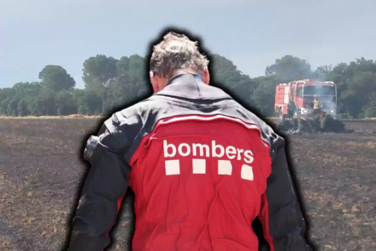 Bomber d’esquena amb jaqueta vermella en un camp cremat i un camió de bombers al fons