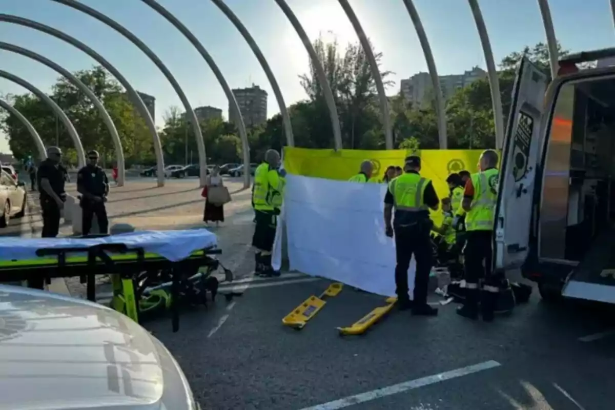 Diversos paramèdics i policies atenen una emergència en un aparcament a l’aire lliure al costat d’una ambulància i una llitera, mentre col·loquen un llençol blanc per cobrir l’escena.