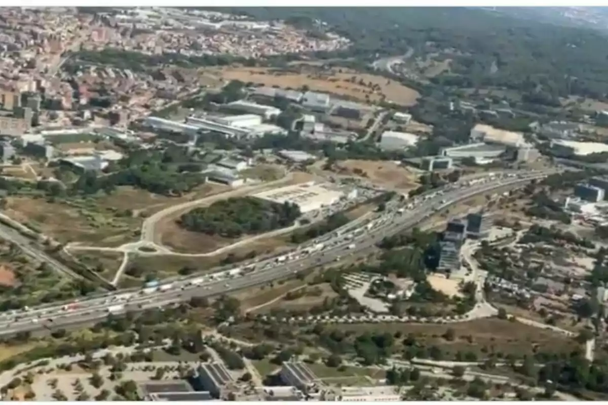 Vista aèria d’una autopista amb trànsit dens envoltada de zones urbanes, edificis i àrees verdes