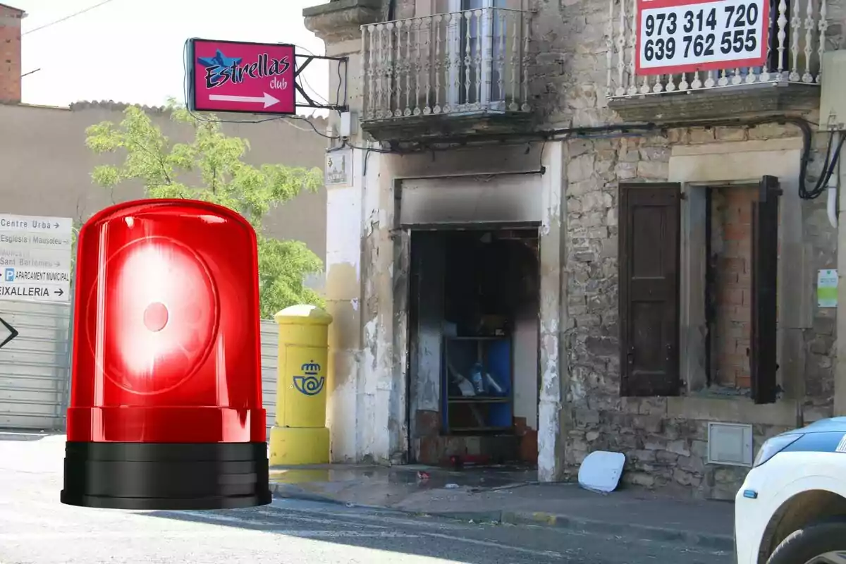 Façana d’un edifici antic amb una porta cremada, una bústia groga de correus, un rètol de club nocturn i una sirena vermella digital superposada en primer pla