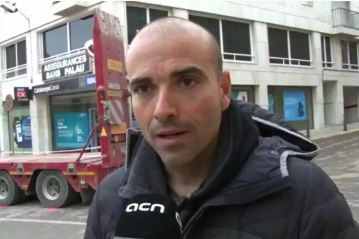 Home calb amb jaqueta fosca sent entrevistat al carrer davant d’un edifici i un camió vermell