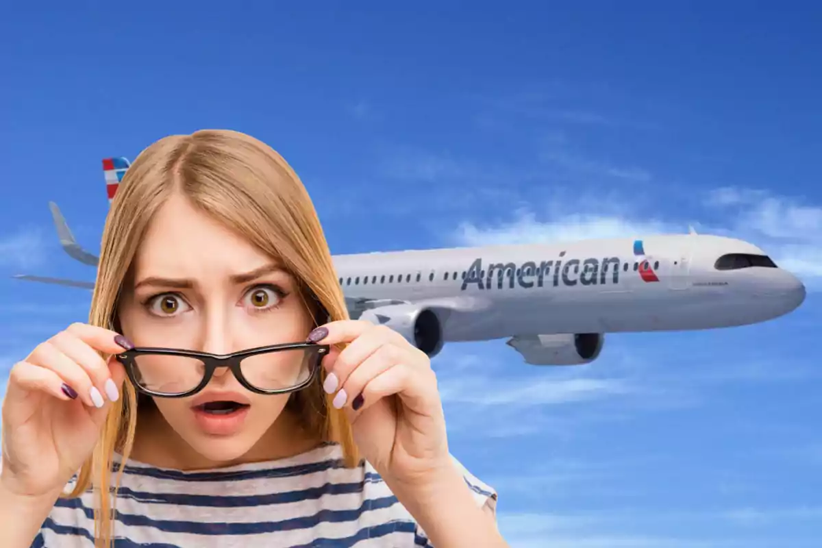 Dona sorpresa amb ulleres en primer pla i un avió d’American Airlines volant pel cel blau de fons Dona sorpresa amb ulleres en primer pla i un avió d’American Airlines volant pel cel blau de fons