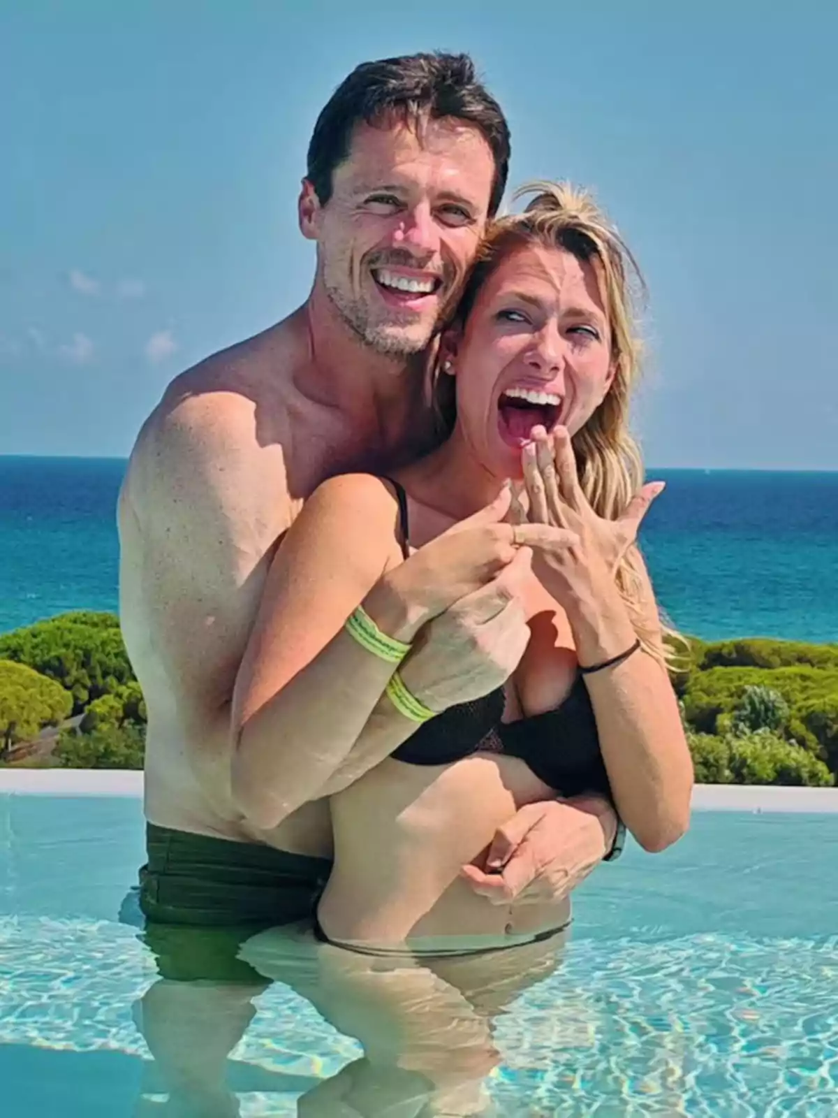 Parella feliç en una piscina amb vista al mar, la dona mostra un anell i tots dos somriuen emocionats. Parella feliç en una piscina amb vista al mar, la dona mostra un anell i tots dos somriuen emocionats.