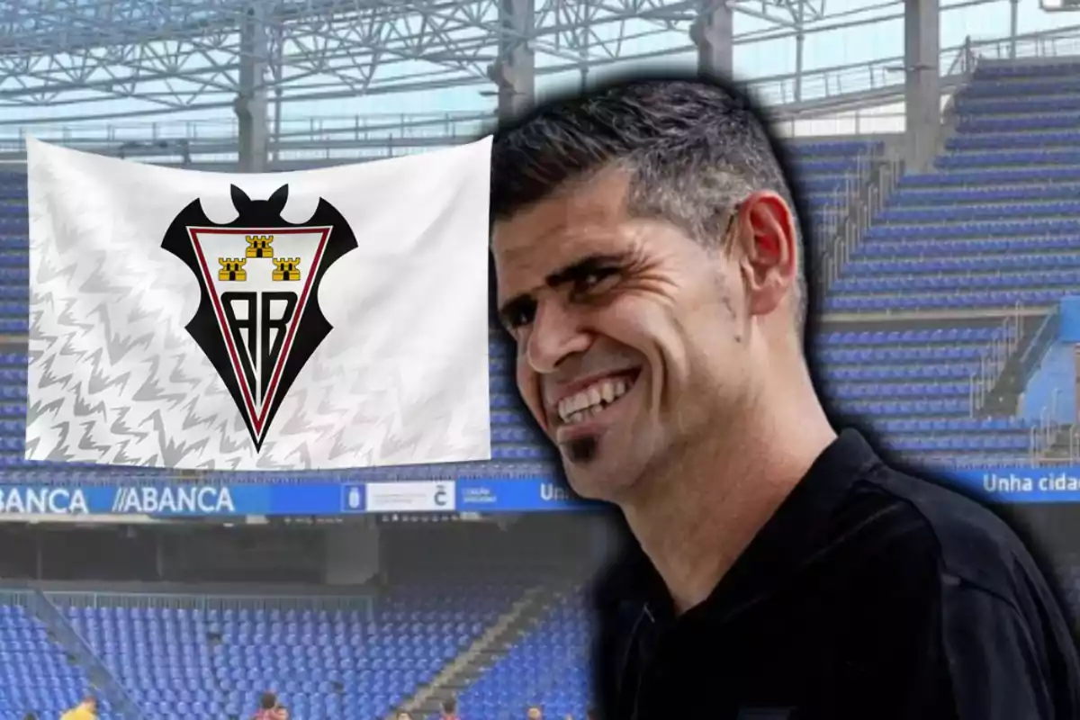 Hombre sonriente en primer plano con una bandera del Albacete Balompié ondeando en un estadio de fútbol vacío