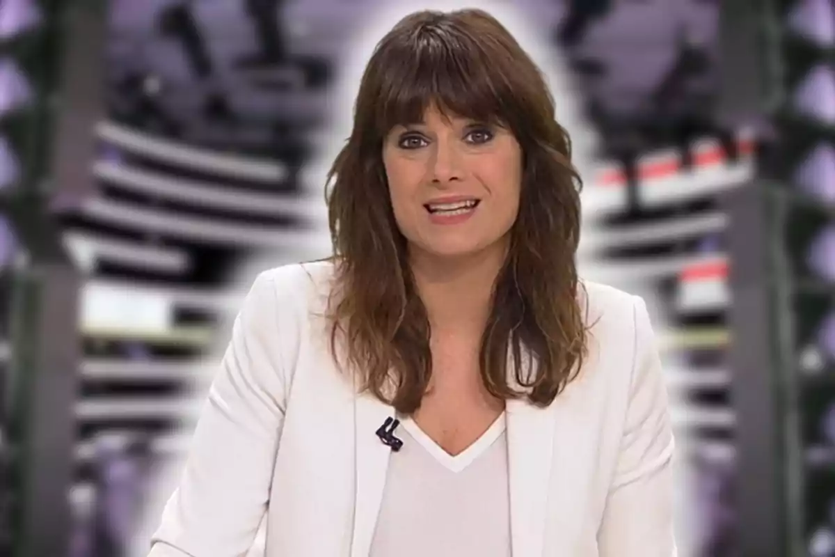Dona de cabells castanys i serrell portant una jaqueta blanca davant d’un fons desenfocat en un estudi de televisió