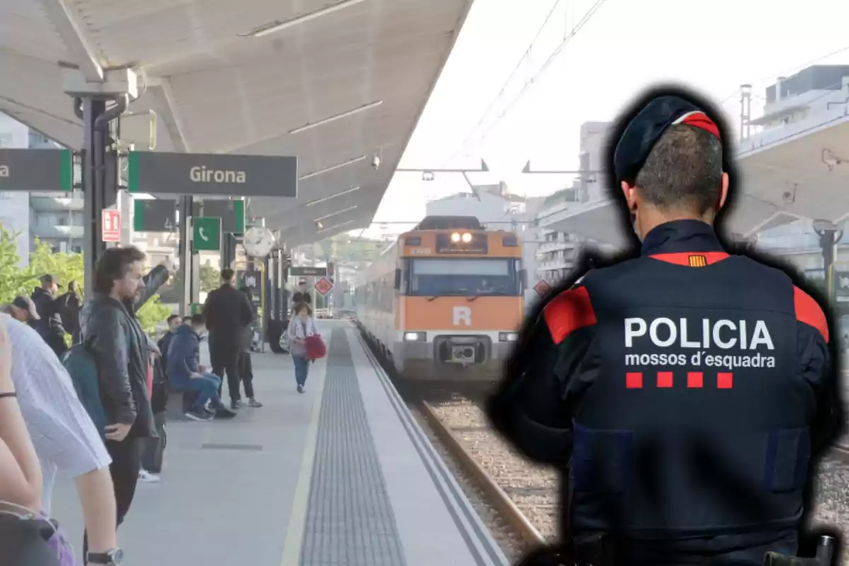 Un agent dels Mossos d'Esquadra d'esquena en primer pla a l'estació de tren de Girona mentre diverses persones esperen a l'andana i un tren s'aproxima.