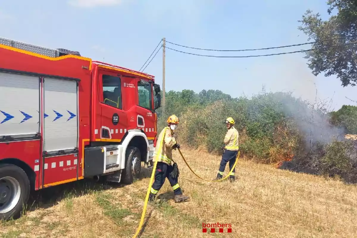 Camión de bomberos y dos bomberos apagando un incendio en un campo seco Camión de bomberos y dos bomberos apagando un incendio en un campo seco