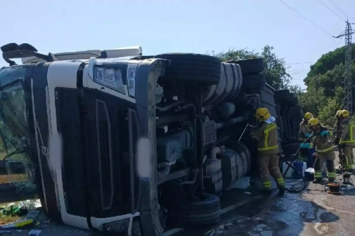 Camió bolcat a la carretera mentre diversos bombers treballen a l’escena de l’accident.