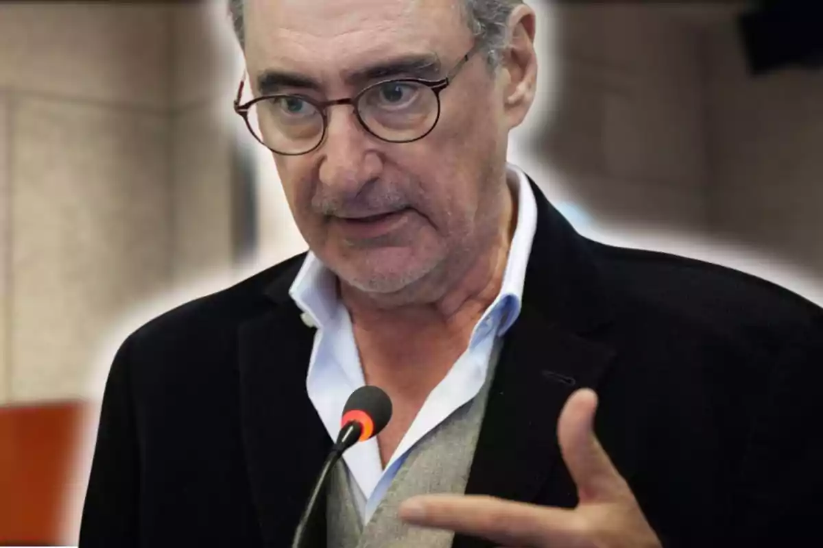 Hombre de mediana edad con gafas y barba canosa hablando frente a un micrófono y gesticulando con la mano
