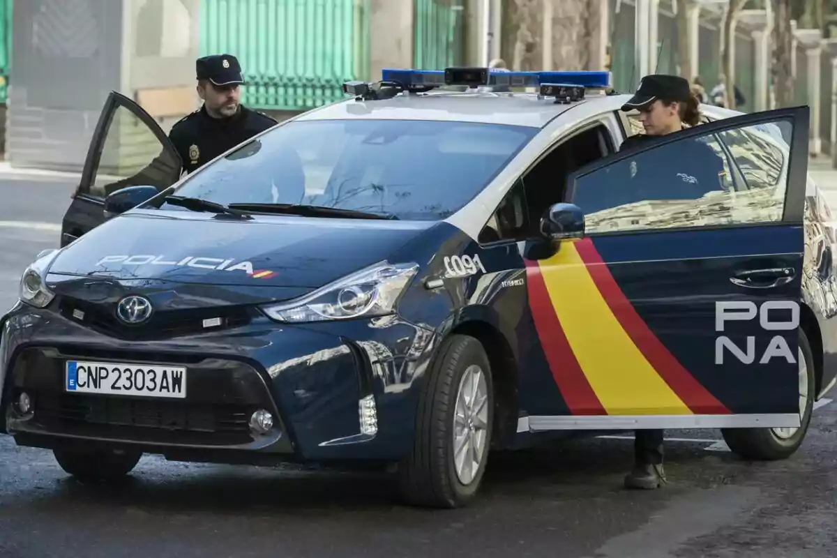 Patrulla de la policia nacional d’Espanya amb dos agents al costat d’un cotxe oficial al carrer Patrulla de la policia nacional d’Espanya amb dos agents al costat d’un cotxe oficial al carrer