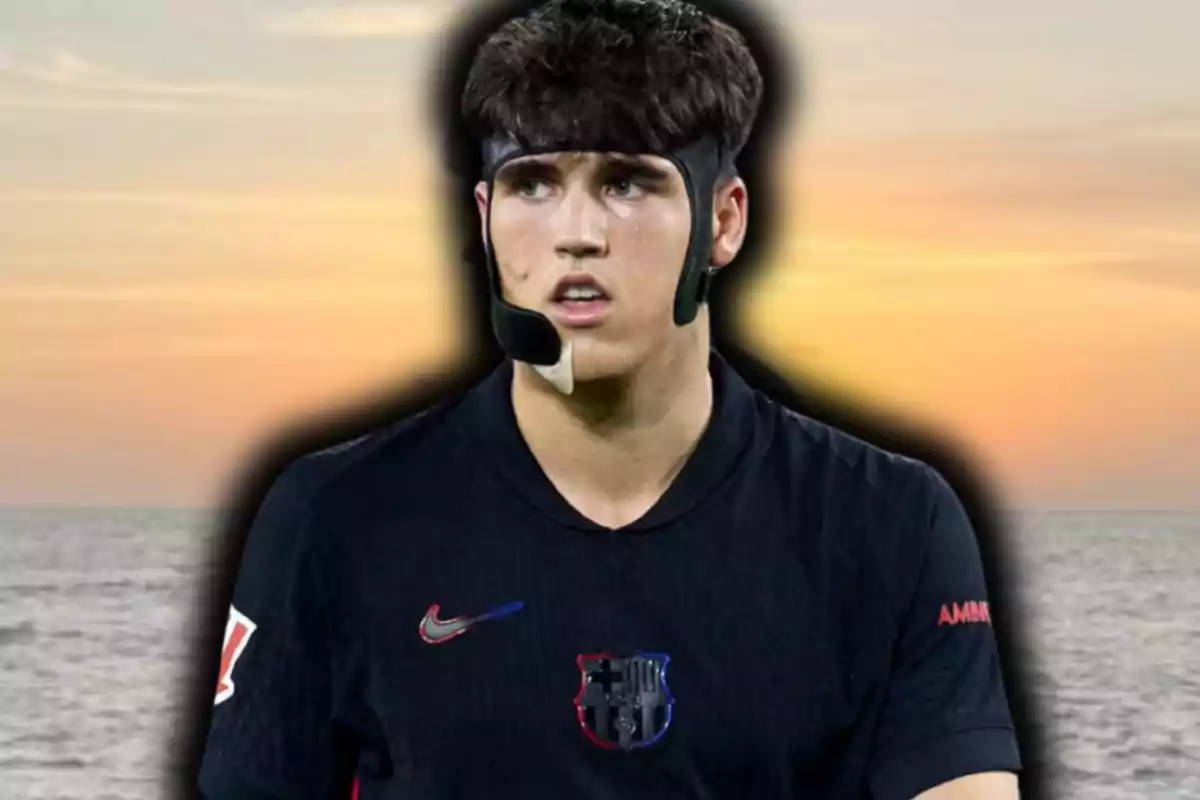 Joven futbolista con protector facial y camiseta negra de un equipo, de pie frente al mar al atardecer