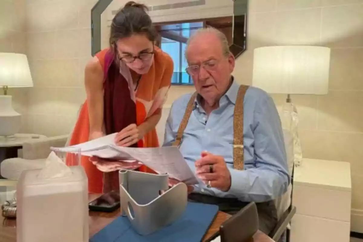 Una dona i un home revisen junts uns documents en una taula dins d’una habitació il·luminada amb làmpades. Una dona i un home revisen junts uns documents en una taula dins d’una habitació il·luminada amb làmpades.