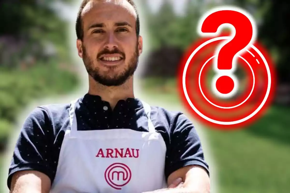 Home amb davantal blanc que porta el nom Arnau i el logotip de MasterChef, dret a l’aire lliure amb un gran signe d’interrogació vermell al seu costat