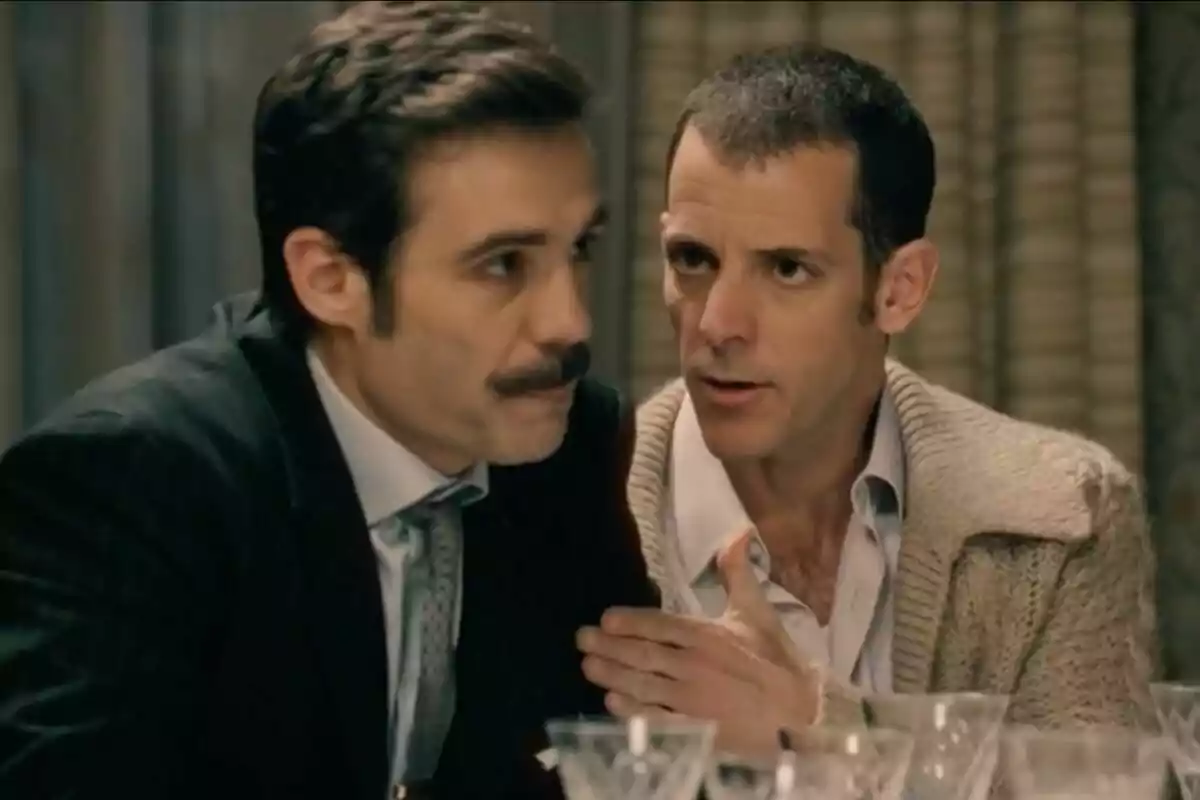 Dos homes conversen en una taula amb copes de vidre al davant, un d’ells porta bigoti —que és Guillermo Barrientos— i vestit, mentre l’altre porta un jersei beix i sembla estar parlant seriosament. Dos homes conversen en una taula amb copes de vidre al davant, un d’ells porta bigoti —que és Guillermo Barrientos— i vestit, mentre l’altre porta un jersei beix i sembla estar parlant seriosament.
