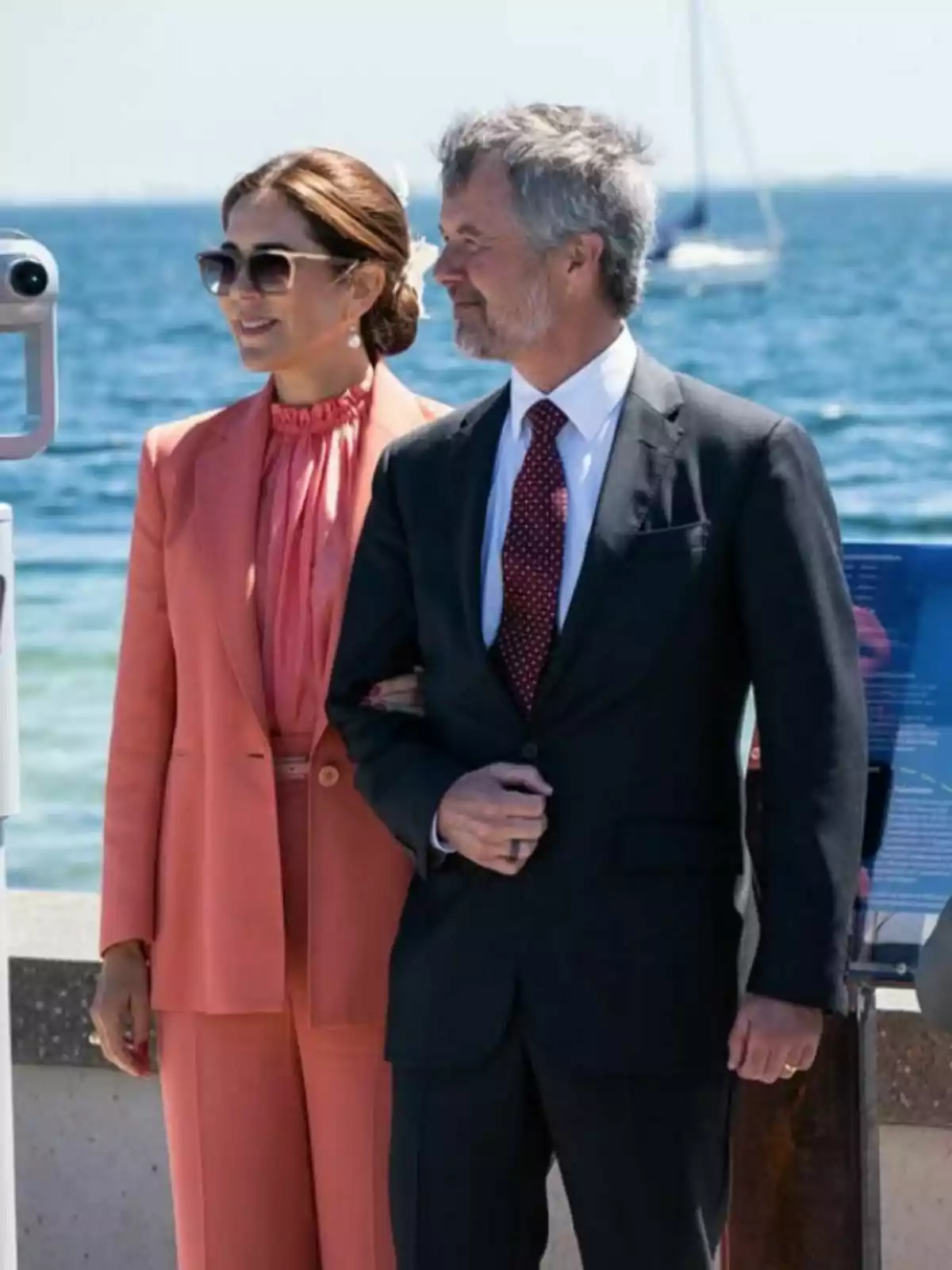 Una pareja elegantemente vestida, que son Federico y Mary de Dinamarca, posa sonriente junto al mar en un día soleado. Una pareja elegantemente vestida, que son Federico y Mary de Dinamarca, posa sonriente junto al mar en un día soleado.