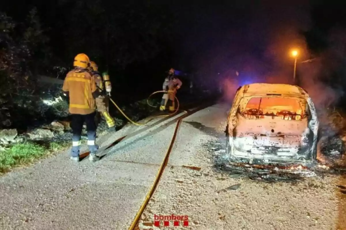 Bombers apaguen un cotxe incendiat en una carretera durant la nit