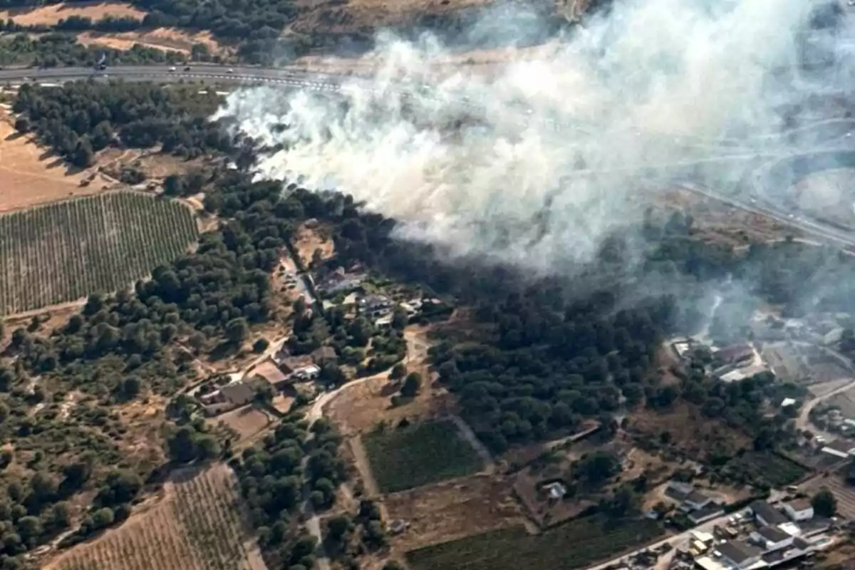 Vista aérea de un incendio forestal cerca de una carretera y zonas habitadas, con humo cubriendo parte del paisaje rural Vista aérea de un incendio forestal cerca de una carretera y zonas habitadas, con humo cubriendo parte del paisaje rural