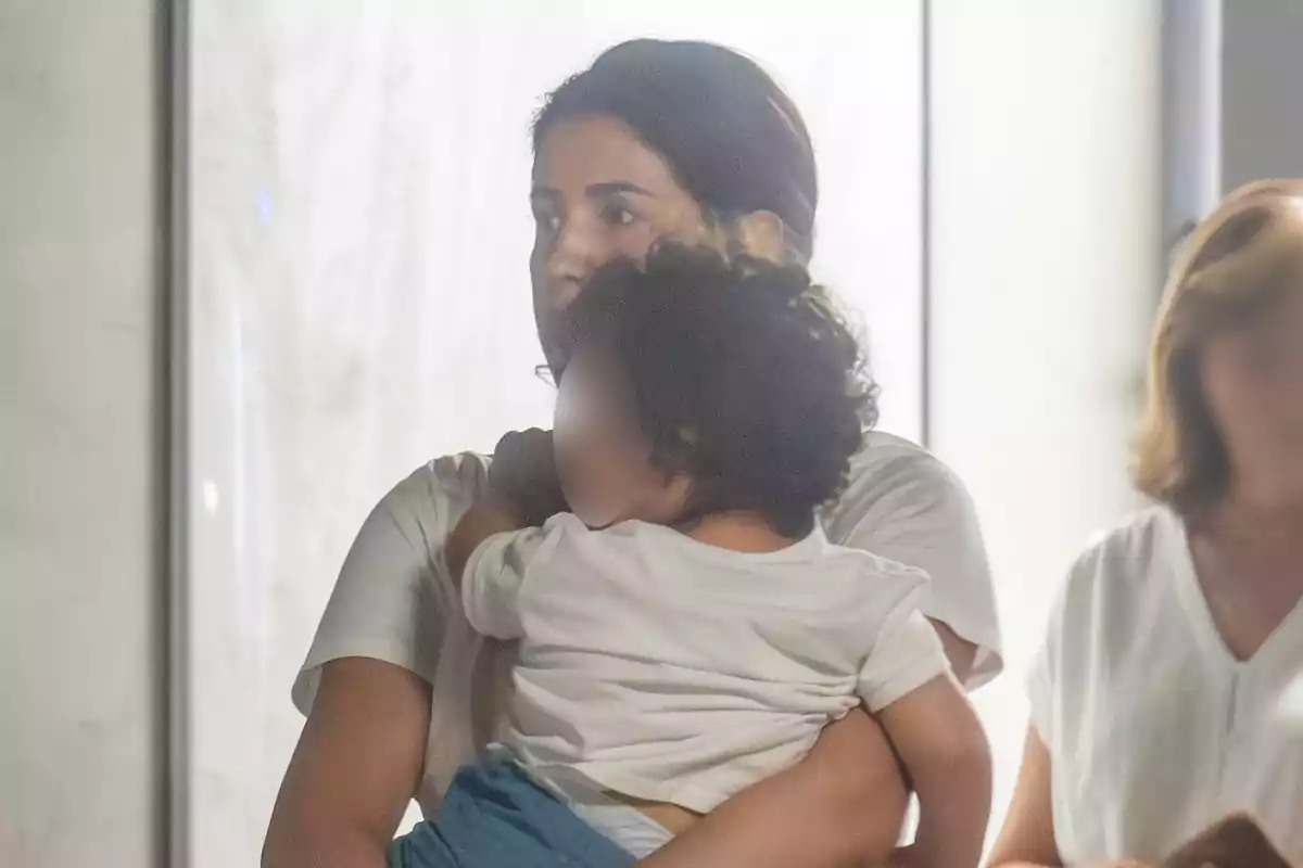 Gabriela Guillén cargando a un niño pequeño con el rostro difuminado en un ambiente interior iluminado Gabriela Guillén cargando a un niño pequeño con el rostro difuminado en un ambiente interior iluminado