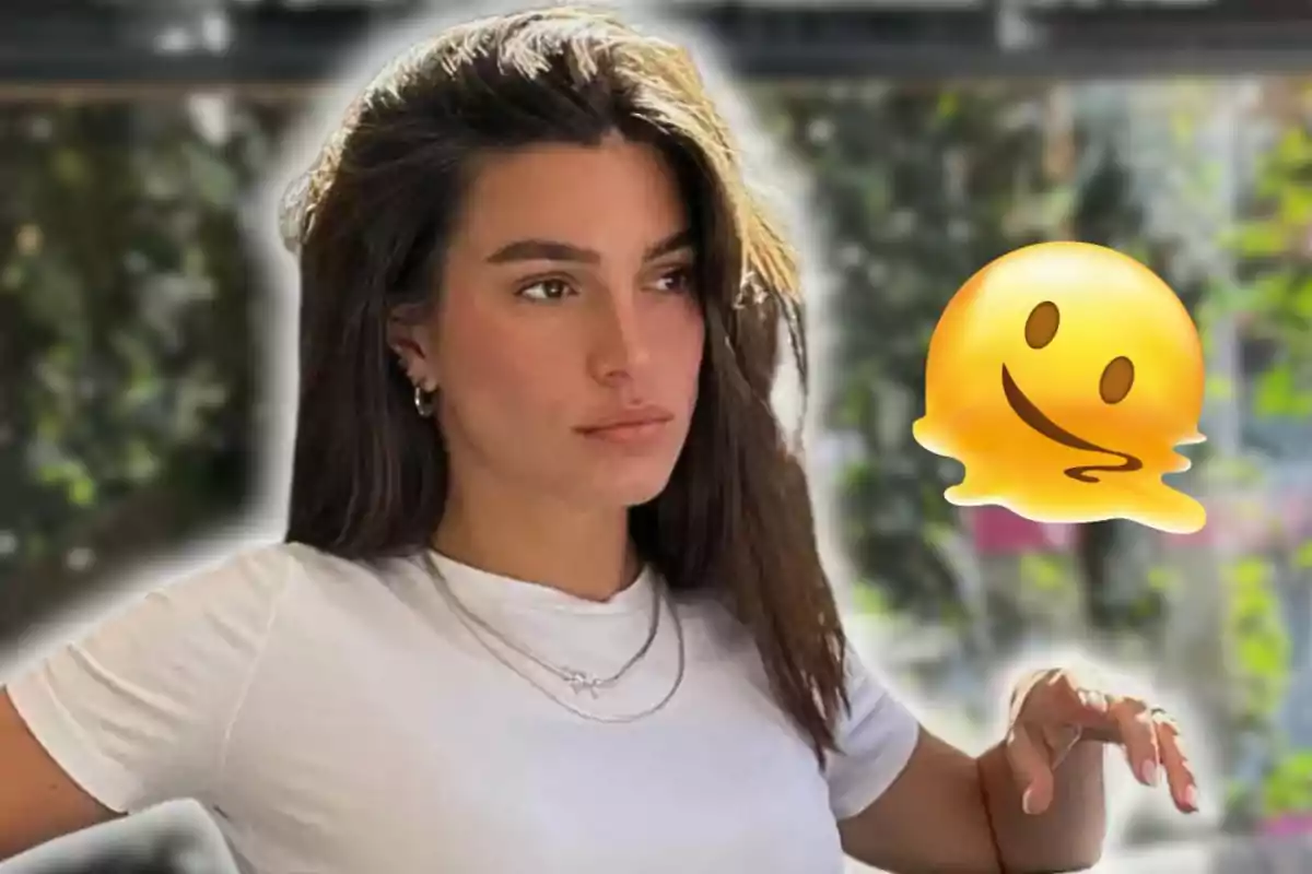 Dona de cabells llargs i foscos amb una samarreta blanca posant al costat d’un emoji groc fos damunt un fons desenfocat de vegetació