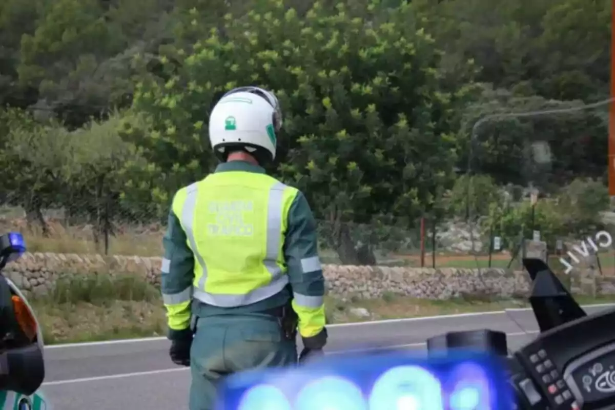 Agente de tráfico con chaleco reflectante y casco de pie junto a una carretera rural rodeada de vegetación y una motocicleta patrulla Agente de tráfico con chaleco reflectante y casco de pie junto a una carretera rural rodeada de vegetación y una motocicleta patrulla