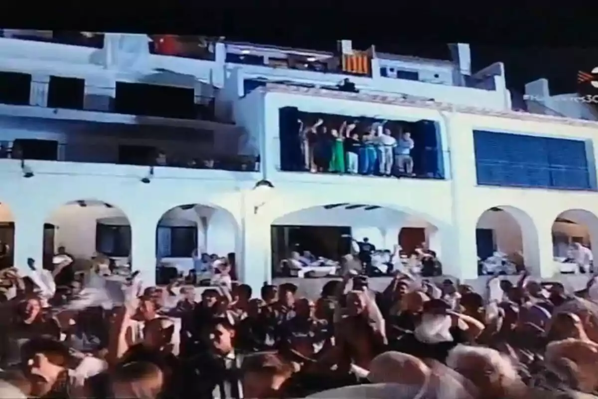 Multitud de persones celebrant al carrer davant d’un edifici blanc amb balcons plens de gent durant la nit Multitud de persones celebrant al carrer davant d’un edifici blanc amb balcons plens de gent durant la nit