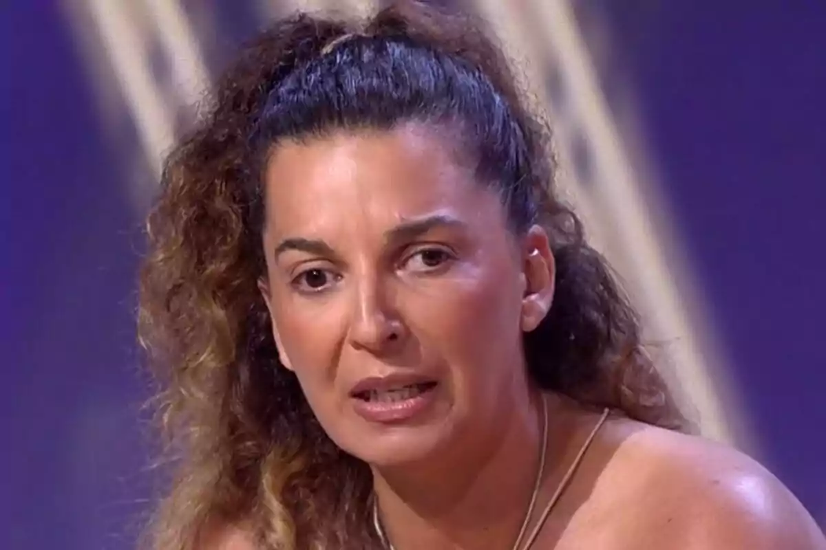 Tamara, hermana de Michu, de cabello rizado recogido con expresión seria en un set de De Viernes con fondo morado. Tamara, hermana de Michu, de cabello rizado recogido con expresión seria en un set de De Viernes con fondo morado.