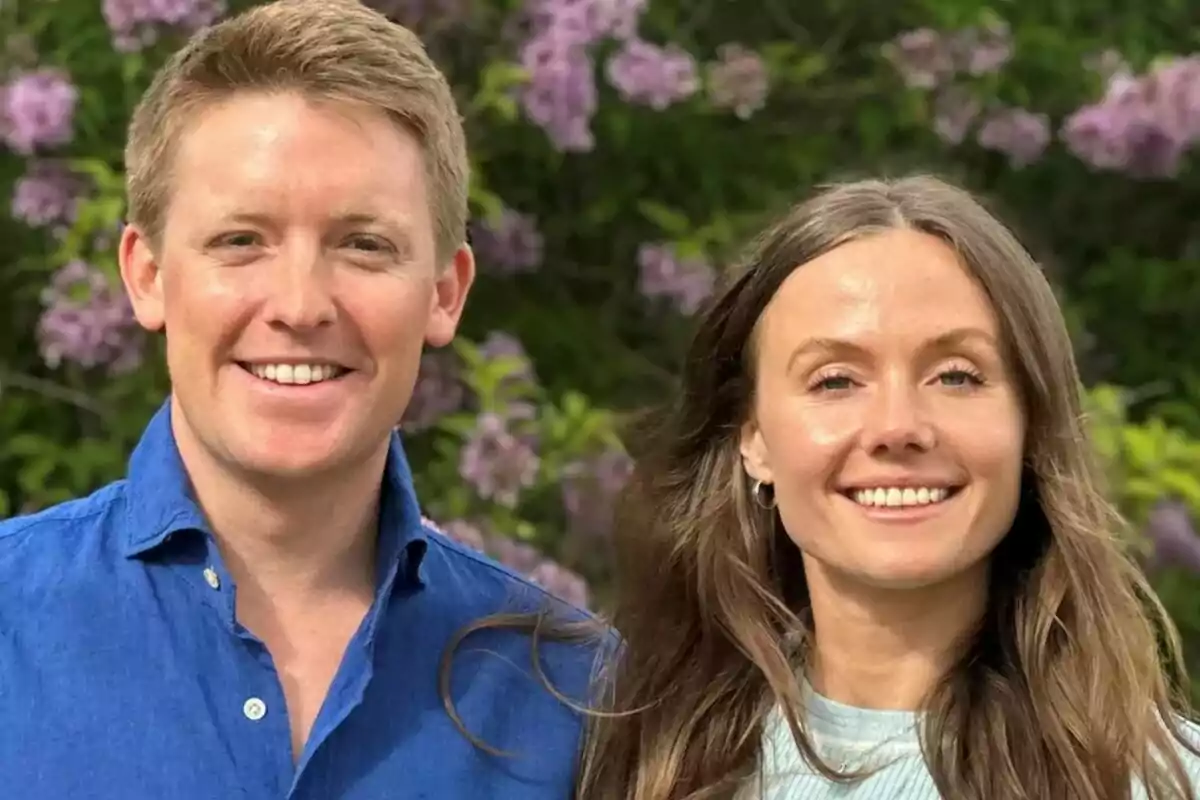 Una pareja sonriente posa al aire libre con flores lilas de fondo Una pareja sonriente posa al aire libre con flores lilas de fondo