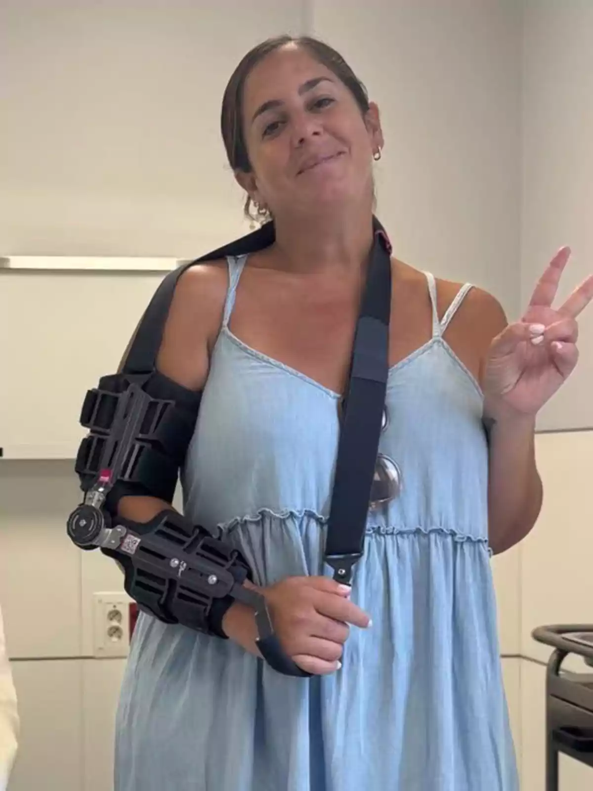 Anabel Pantoja con vestido azul claro usando un inmovilizador ortopédico en el brazo derecho y haciendo el signo de la paz con la mano izquierda en una sala blanca Anabel Pantoja con vestido azul claro usando un inmovilizador ortopédico en el brazo derecho y haciendo el signo de la paz con la mano izquierda en una sala blanca