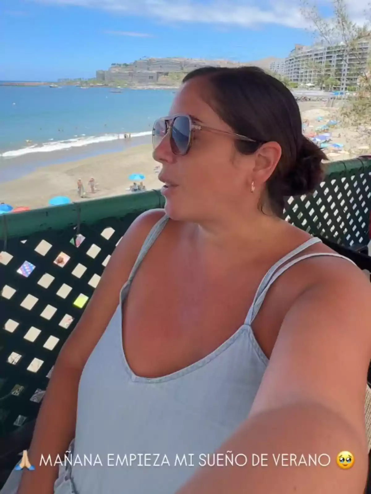 Anabel Pantoja con gafas de sol y vestido claro tomándose una selfie en una terraza frente a la playa con sombrillas y edificios al fondo Anabel Pantoja con gafas de sol y vestido claro tomándose una selfie en una terraza frente a la playa con sombrillas y edificios al fondo