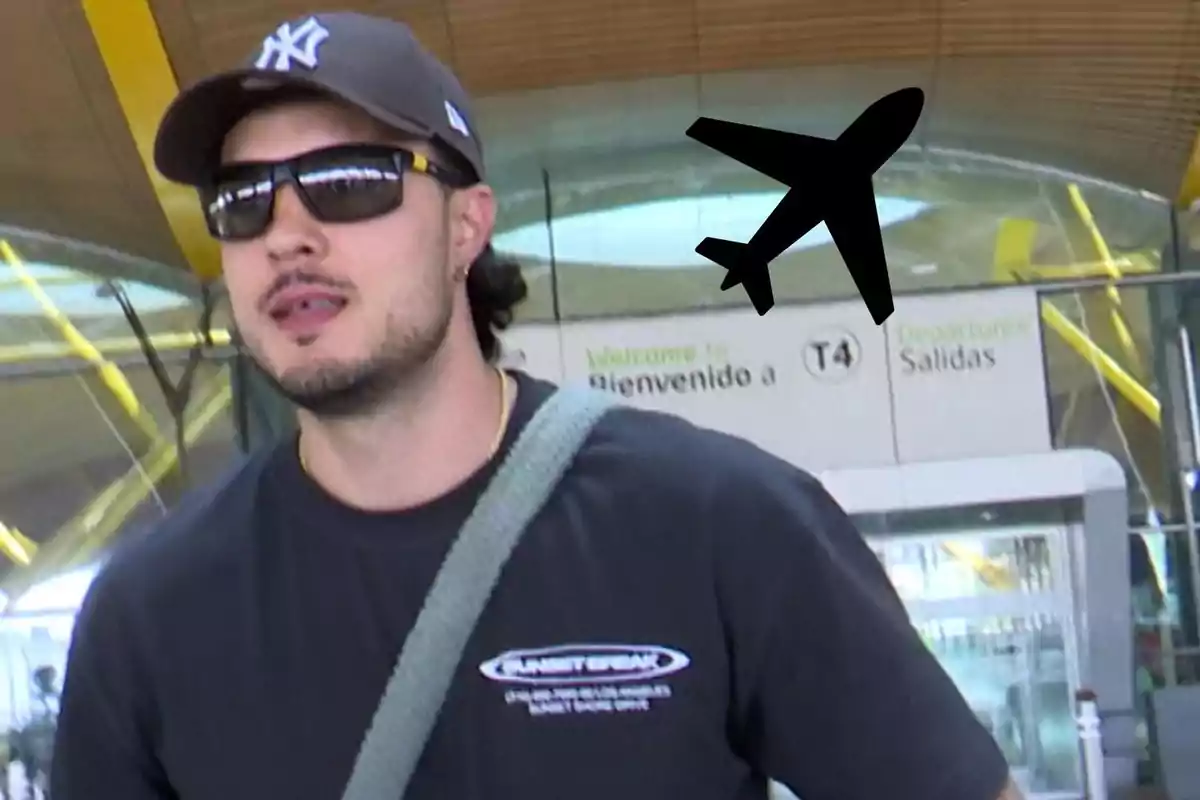 Carlo Costanzia con gorra y gafas de sol en un aeropuerto con un dibujo de avión negro al fondo y letrero de bienvenida a la terminal T4.