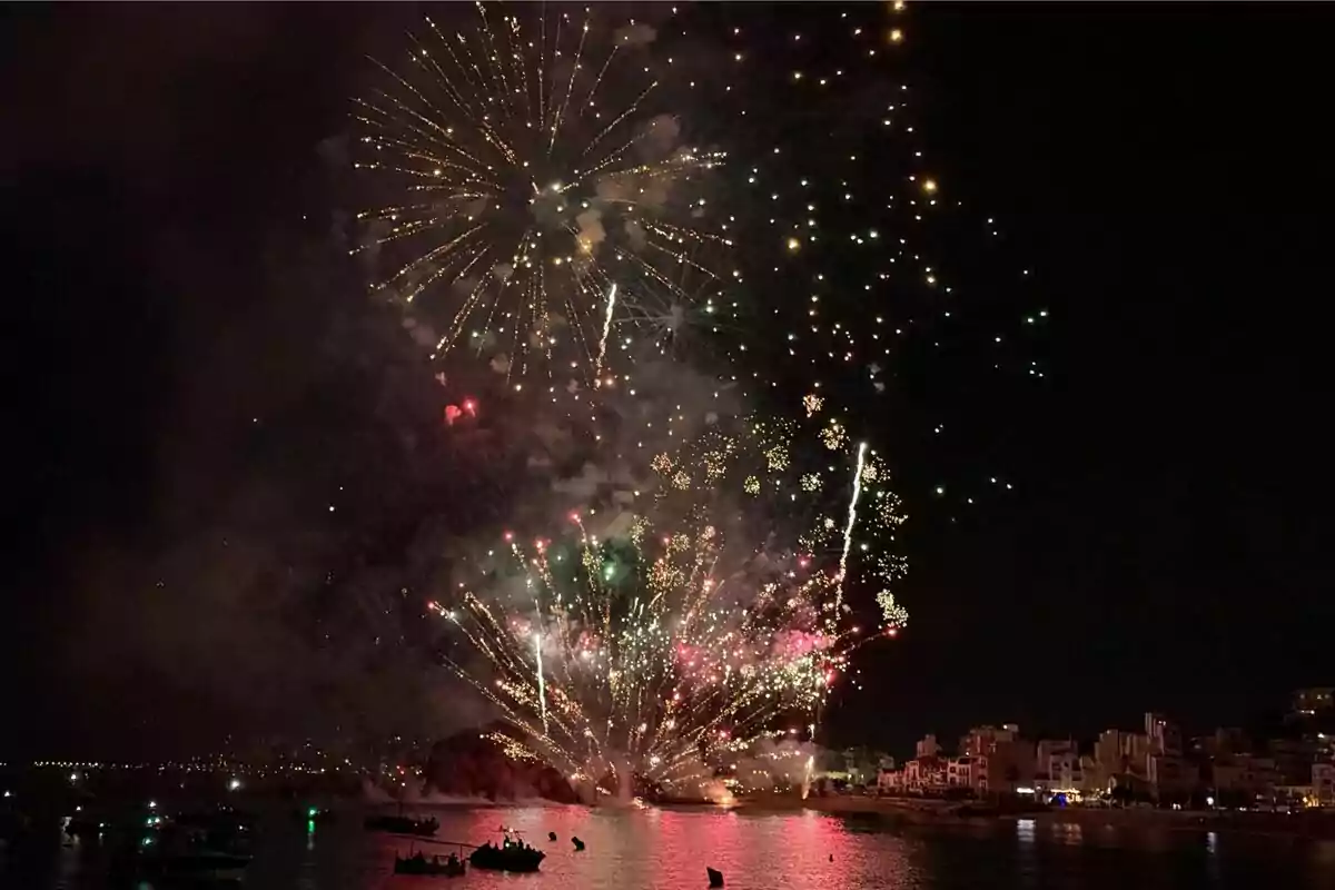 Focs artificials il·luminen el cel nocturn sobre una ciutat costanera mentre es reflecteixen a l’aigua i diverses embarcacions observen l’espectacle. Focs artificials il·luminen el cel nocturn sobre una ciutat costanera mentre es reflecteixen a l’aigua i diverses embarcacions observen l’espectacle.