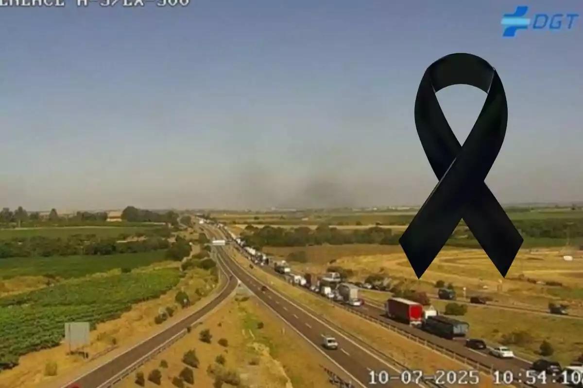 Carretera amb trànsit dens en un entorn rural i un llaç negre de dol a la cantonada superior dreta