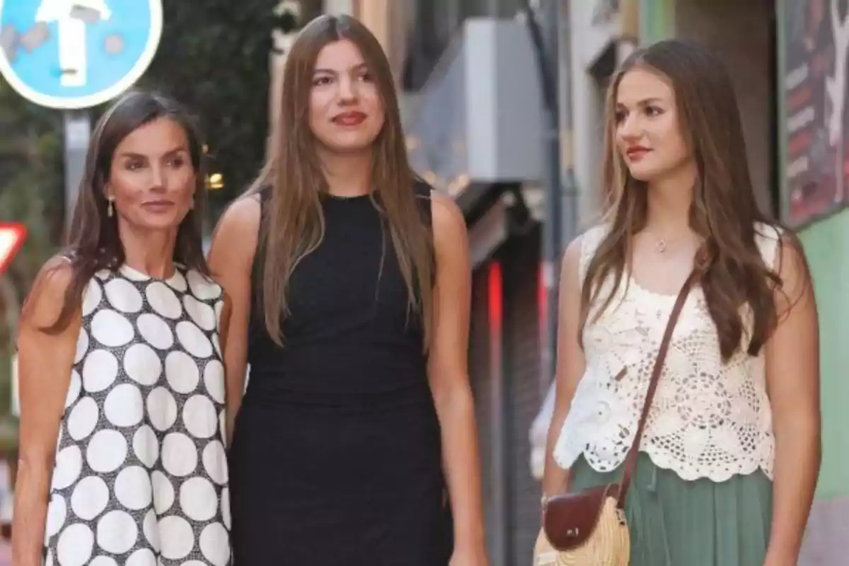 Tres dones joves posen juntes en un carrer, lluïnt roba d’estiu i somrient suaument. Tres dones joves posen juntes en un carrer, lluïnt roba d’estiu i somrient suaument.